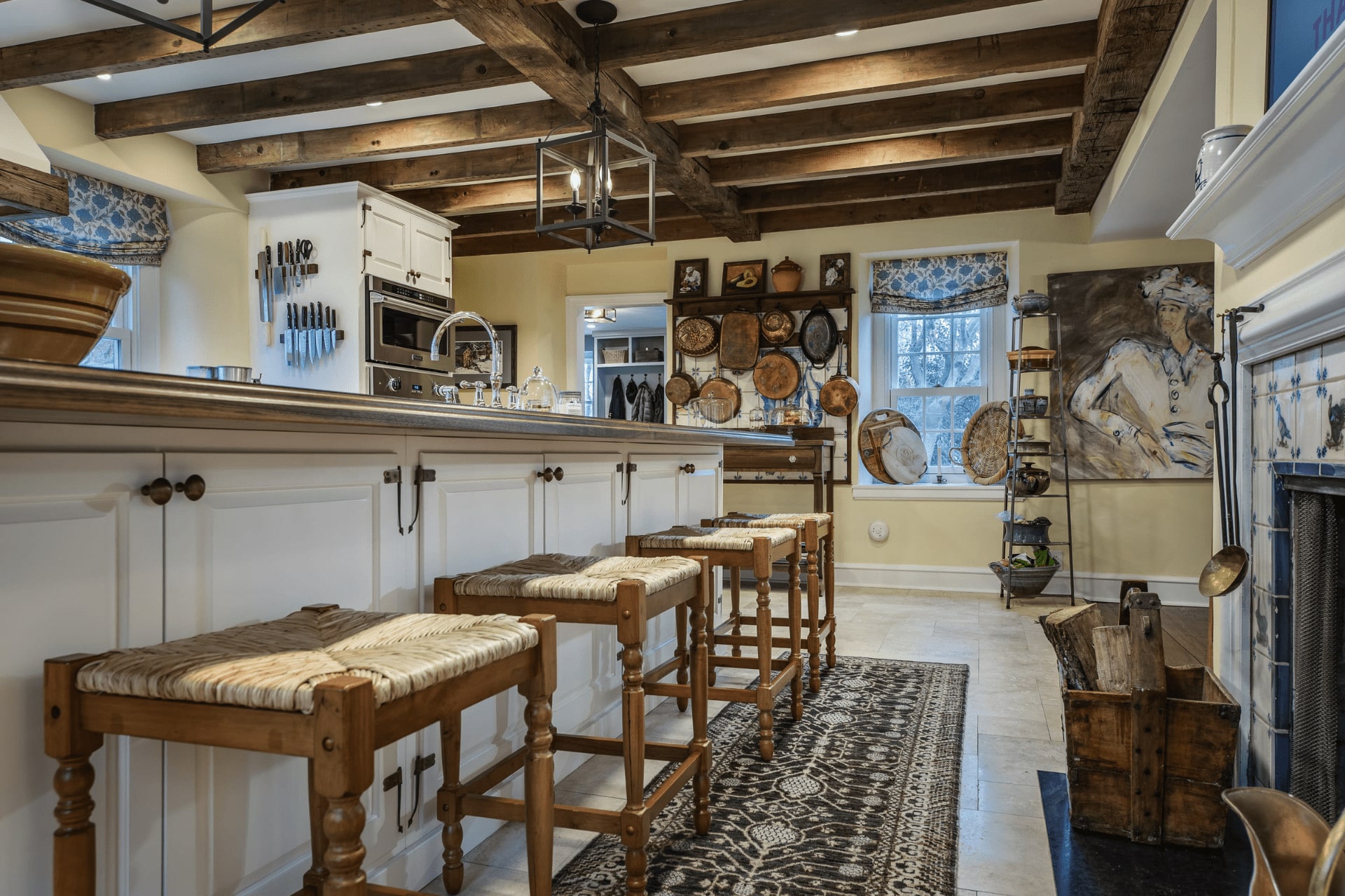 A spacious kitchen features a wooden island with chairs, modern appliances, and rustic decor. Natural light filters through windows, highlighting wooden beams and a cozy, inviting atmosphere.