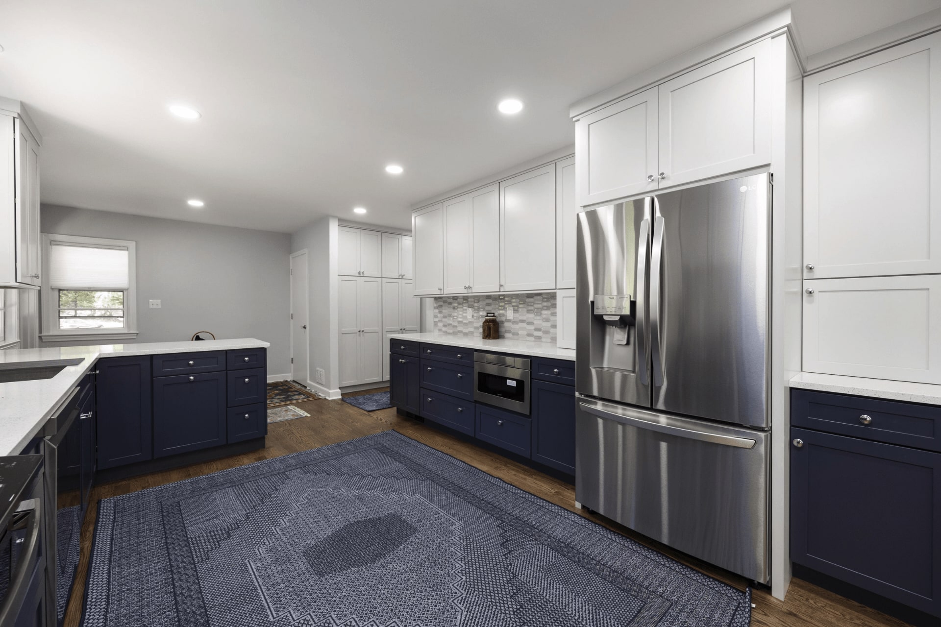 A modern kitchen features navy blue cabinetry and stainless steel appliances. The countertop displays a sleek design, and an area rug with a geometric pattern enhances the warm wood flooring.