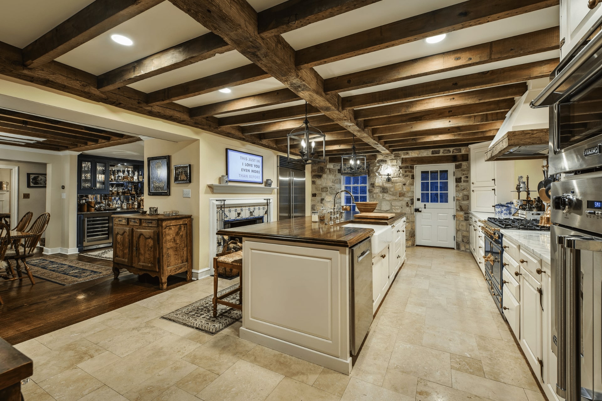 A spacious kitchen features an island with a wooden countertop, while a cozy dining area with traditional chairs sits nearby. Exposed beams and stone walls enhance the rustic ambiance.