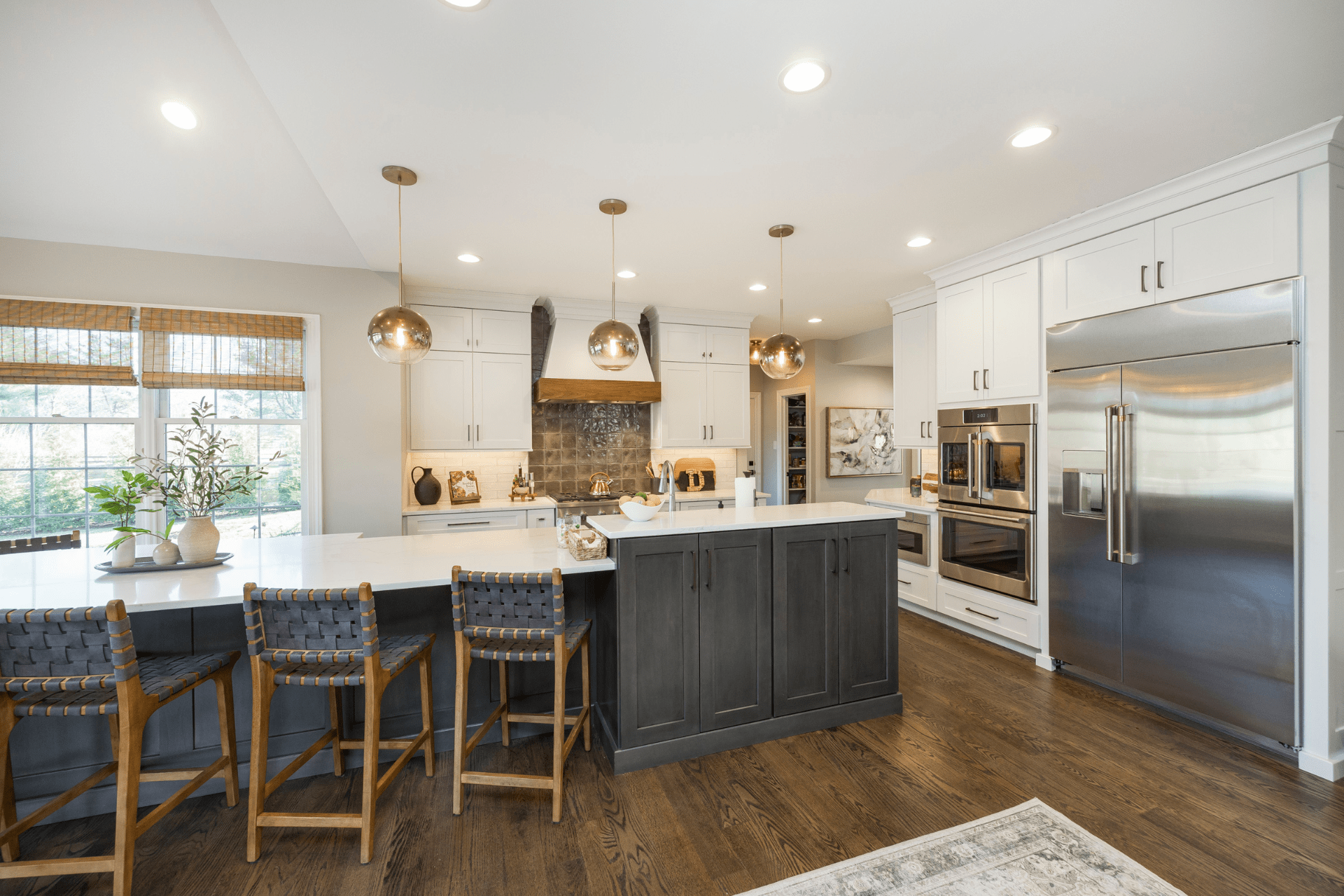 A sleek kitchen features a central island with bar stools, pendant lights overhead, and stainless steel appliances. Natural light filters through windows, illuminating the modern design and warm wood flooring.