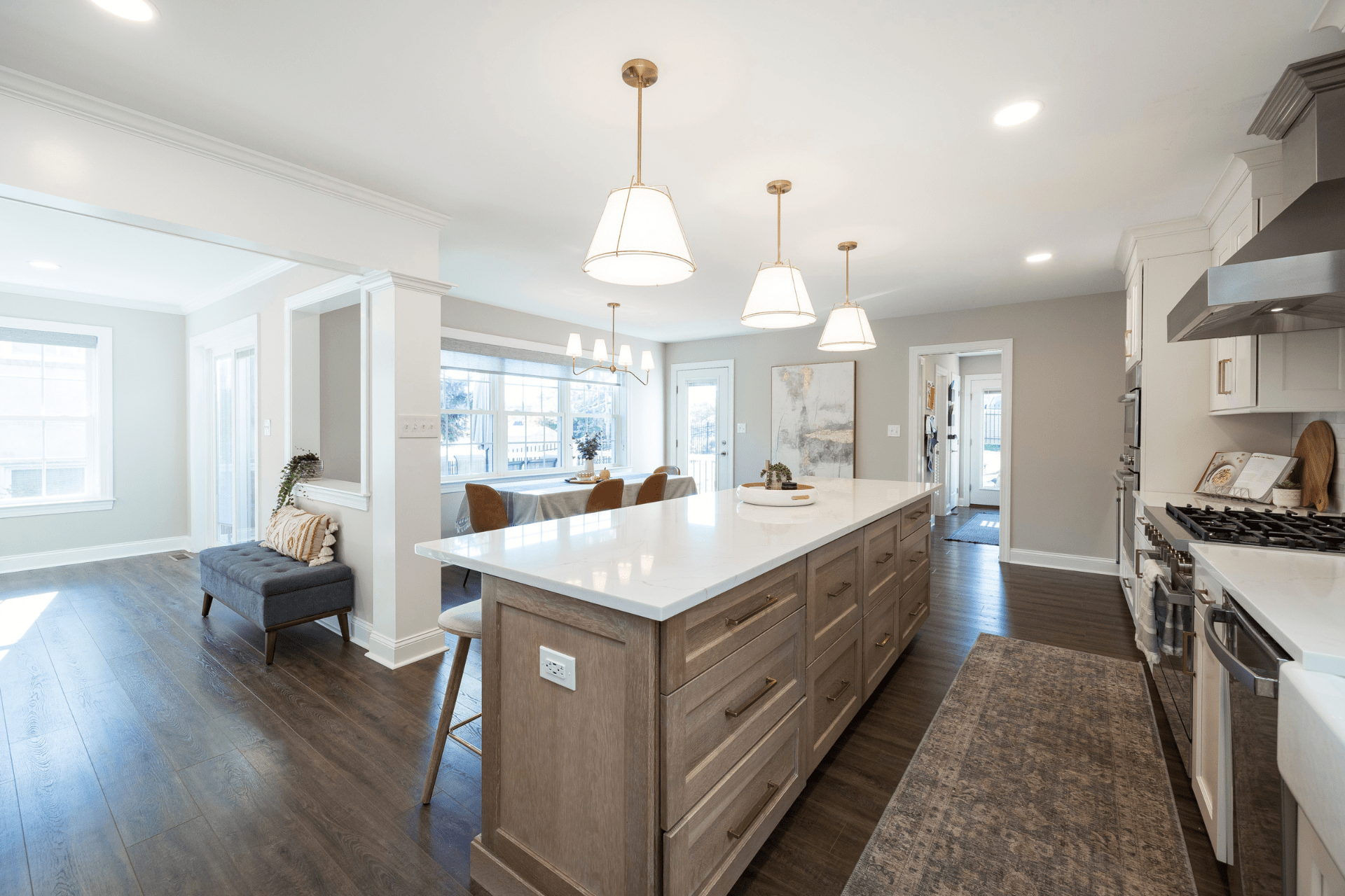 A modern kitchen features a large central island with drawers and a countertop, 3 pendant lights above, and an open layout connecting to a dining area with a table and chairs.