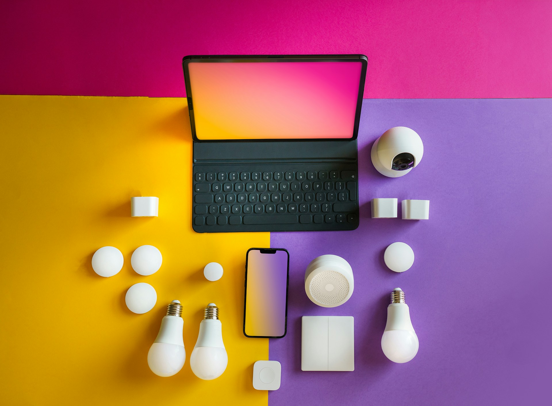 A tablet with keyboard, a smartphone, smart bulbs, cameras, plugs, and other smart home devices are arranged on a colorful pink, yellow, and purple background.
