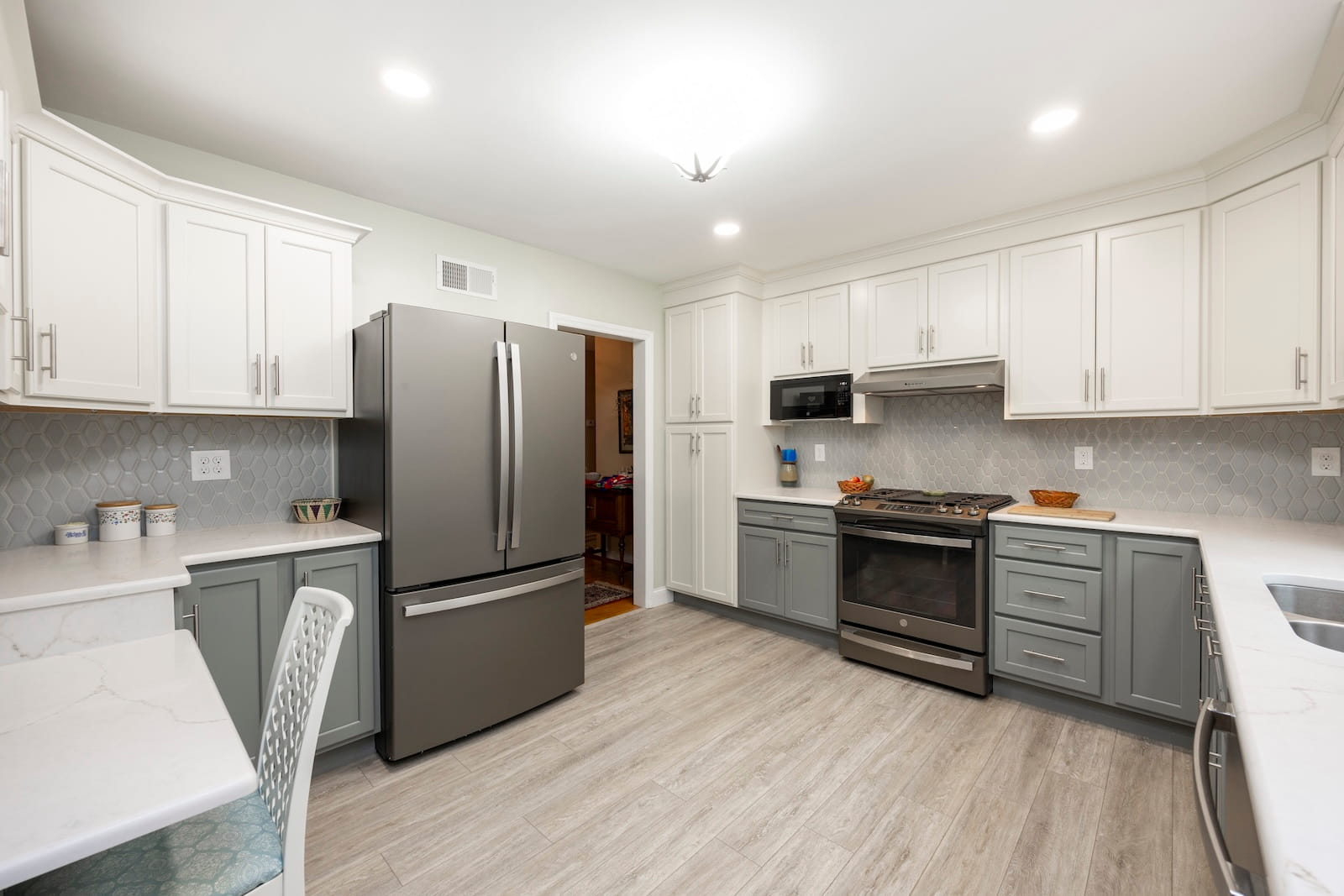 Modern kitchen with white upper cabinets, gray lower cabinets, stainless steel appliances, light wood flooring, and a geometric tile backsplash. Marble countertops and recessed lighting create a bright, clean space.
