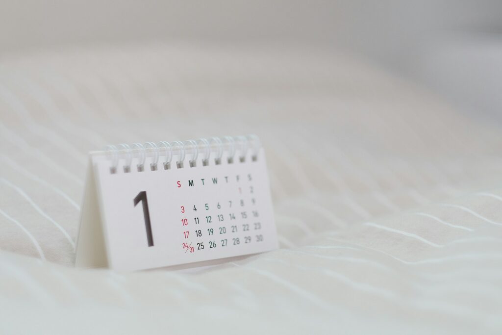 A small desk calendar open to the month of January sits on a light-colored, striped fabric surface. The dates are clearly visible, and the background is softly blurred.